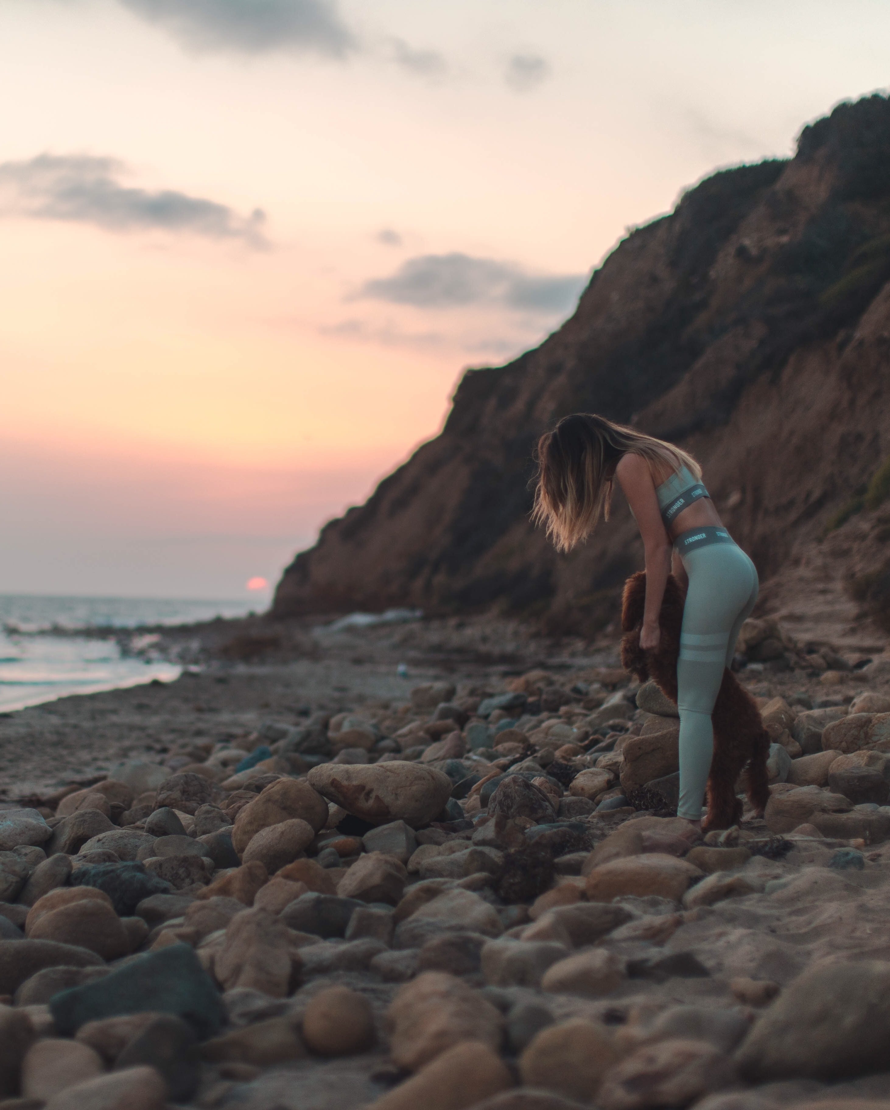 Labradoodle puppy with girl on rocky beach sunset